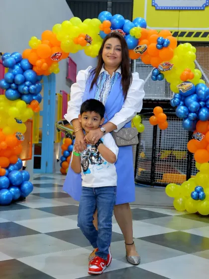 A mother and the birthday boy pose in front of a vibrant 'Hot Wheels' themed balloon arch, ready to celebrate the big day.