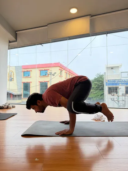 A student practices Bakasana (Crow Pose), a foundational arm balance that builds upper body strength and confidence.