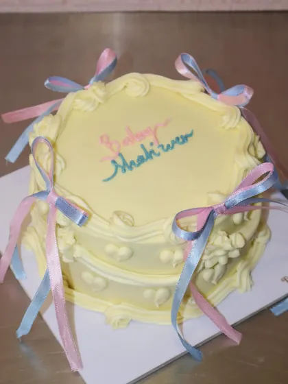 A full view of the two-tiered vintage baby shower cake with its delicate ribbon bows and classic piping.