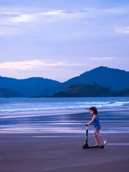 The simple joy of a child riding a scooter on the beach at dusk. The vastness of the sea and sky creates a beautiful sense of scale and freedom.