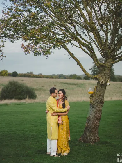 A sunny Haldi ceremony in the British countryside, with details like "Love is all we need" henna, fresh yellow flowers, and bowls of rose petals.