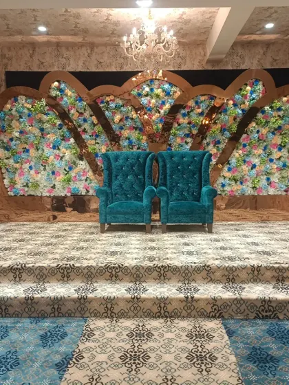 A grand reception stage with two high-back teal chairs set against a massive floral backdrop in the shape of wings. This bold design at Emerald Door banquet makes a powerful statement.