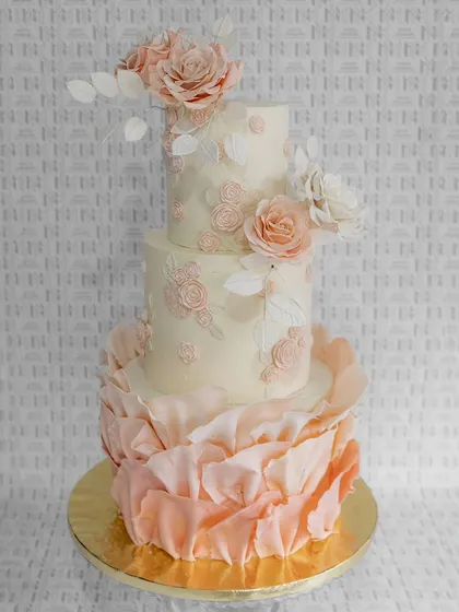 Ruffles and roses create a vision of romance. This three-tiered wedding cake combines soft, flowing ruffles on the bottom tier with delicate stenciling and fresh roses on top.