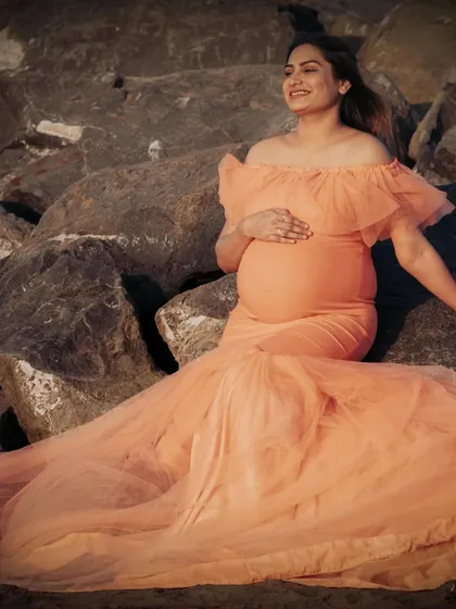 Relaxing on the rocks by the sea, this mom-to-be shines in the peach mermaid gown. The flowing tulle train spreads out beautifully, creating a gorgeous composition.