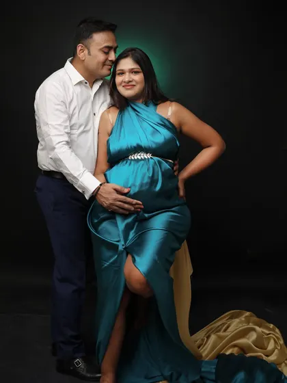 This portrait highlights a glamorous look with a satin teal gown that has a high slit. The couple's pose is both intimate and confident, captured against a classic dark studio background.