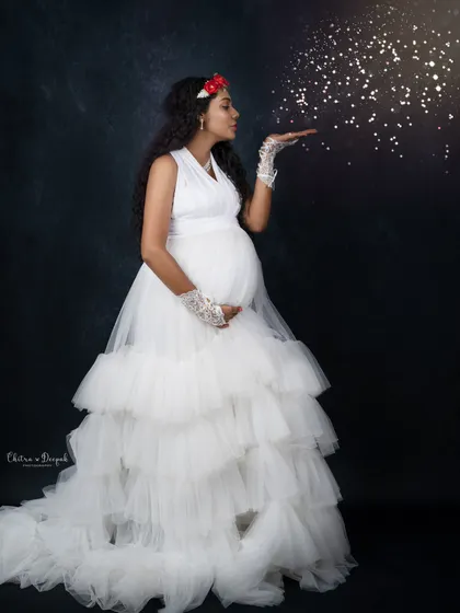Blowing a little magic. This whimsical shot features a mom-to-be in a white ruffled gown, blowing sparkling glitter for a fairytale effect.