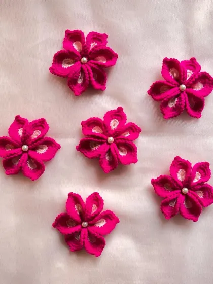 A set of bright pink flowers, each with a small pearl at its center. These can be used as decorative accents on clothing, bags, or for craft projects.