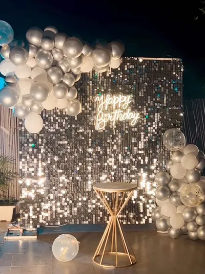 A minimalist and chic outdoor birthday backdrop. A silver shimmer wall is framed by a simple silver and white balloon arrangement.