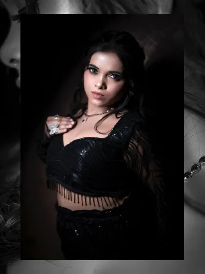 A mid-shot portrait focusing on the texture of the fringed top and the model's direct, confident gaze. The dark, moody lighting enhances the glamour of this studio fashion shot.