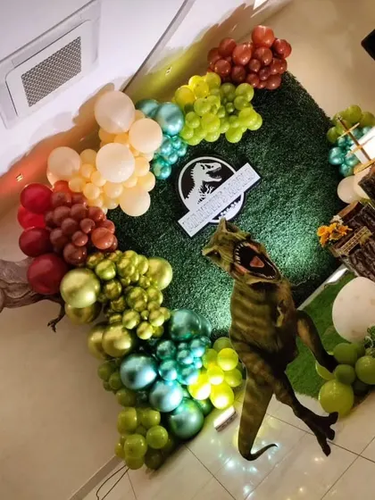 A top-down angle of the dinosaur decor, showing the texture of the balloon garland against the grass wall.
