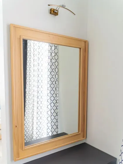 A simple, elegant wooden-framed mirror in the kid's room, with a picture light above it, adding a touch of sophistication.
