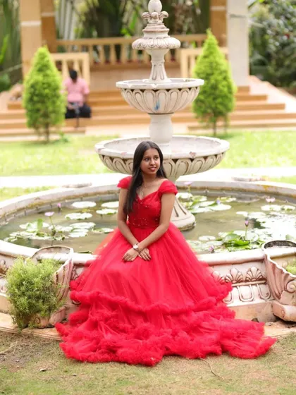 Another beautiful shot of our client enjoying her photoshoot in the red gown, showcasing its elegance in a serene garden setting.