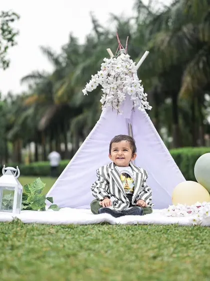 A wide view of our outdoor picnic setup for a first birthday. The teepee, 'ONE' sign, and lanterns create a picturesque scene against the backdrop of palm trees.