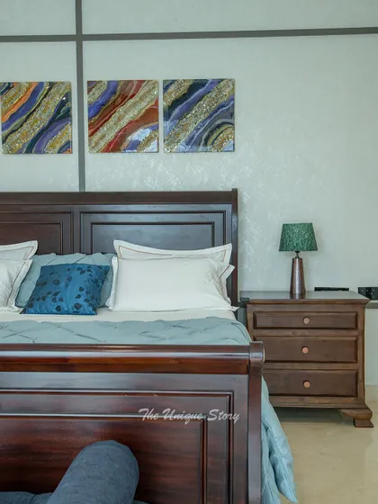 A close-up of a classic sleigh bed in a dark wood finish. Above the bed, a triptych of abstract resin art adds a pop of color and modern flair to the traditional furniture.