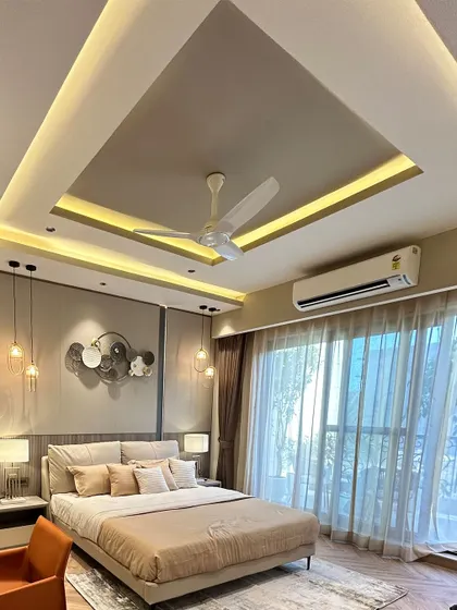 A full view of the luxurious beige bedroom, showing the elegant false ceiling design with integrated cove lighting that enhances the room's spacious and airy feel.