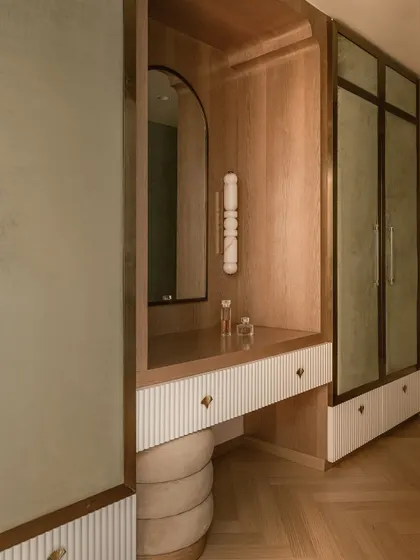 The walk-in closet and vanity area, designed with warm oak, ribbed white panels, and sage green velvet accents. The space is a refined mix of elegance and playfulness.