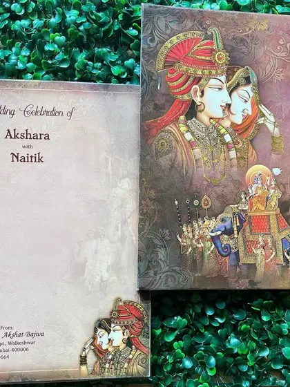 This invitation features a beautiful painting of a royal couple and a baraat procession, capturing the grandeur and romance of a traditional Indian wedding.