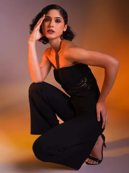 A powerful, low-angle squatting pose. The colored lighting from both sides sculpts the model's form and creates a dynamic, high-fashion look.