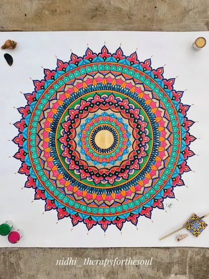 The 'Rainbow Riot' mandala laid out on the ground, surrounded by some of the paint pots used to create its vibrant, multi-colored design.