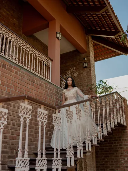 A full-length shot of the bride on a staircase with intricate railings, her white lehenga creating a stunning visual against the brick architecture.