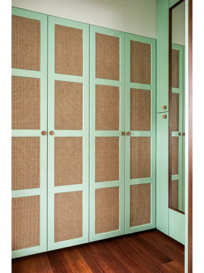 Adjacent to the studio is a walk-in wardrobe with custom mint green and rattan cane shutters, continuing the color theme while providing ample, breathable storage.