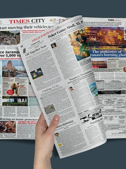 A stylized photo of a hand holding the Times City newspaper, with the feature on the Varanasi ghats prominently displayed. This image emphasizes the public recognition of our work in civic architecture.