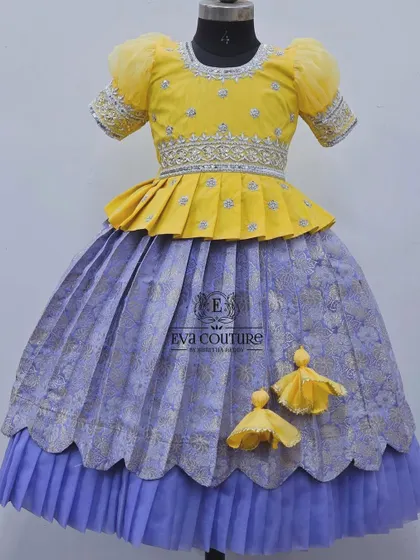 A soft yellow peplum top with silver embroidery, paired with a lavender pleated skirt. The skirt has a double-layered hem for a modern, ruffled look.