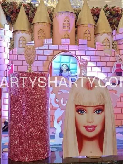 A detailed shot of a Barbie castle backdrop, complete with pink glitter towers and large cutouts of Barbie, perfect for a themed cake-cutting ceremony.