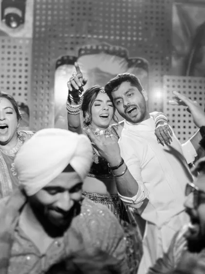 The raw energy of the Mehendi party captured in a candid black and white shot, showing the couple and guests dancing without inhibition.