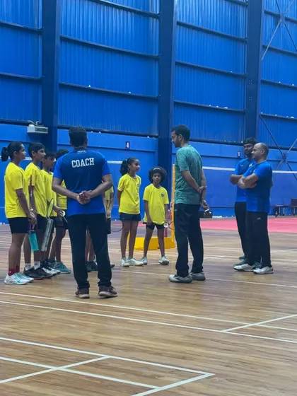 A huddle on the court where Mr. Gopichand provides direct feedback and strategy to a group of young players and coaches.