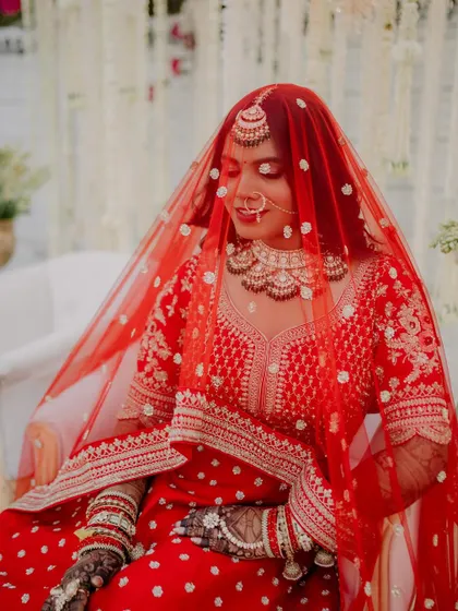 The red veil adds a touch of tradition and mystery to this beautiful portrait. The makeup remains flawless and radiant, capturing the essence of her bridal look.