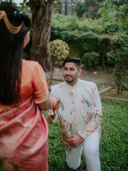 The groom-to-be on one knee, presenting the ring during an outdoor engagement photoshoot.