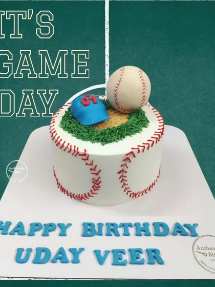It's game day! A baseball-themed cake designed to look like a baseball, complete with red stitching, a cap, and a grassy field on top.