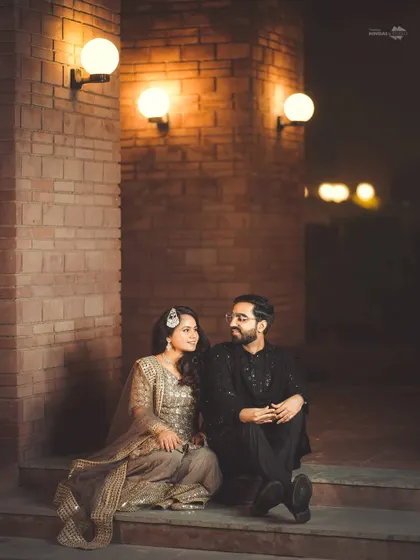 An intimate moment during a Sangeet night. The couple shares a quiet conversation under the warm glow of wall lights, a peaceful pause in the middle of the celebration.
