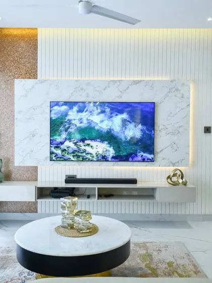This sleek TV unit is set against a marble-clad wall and glows with soft backlighting. The combination of textured metallic panels, sheer curtains, and modern decor creates a look that is simple, fresh, and perfectly put together.