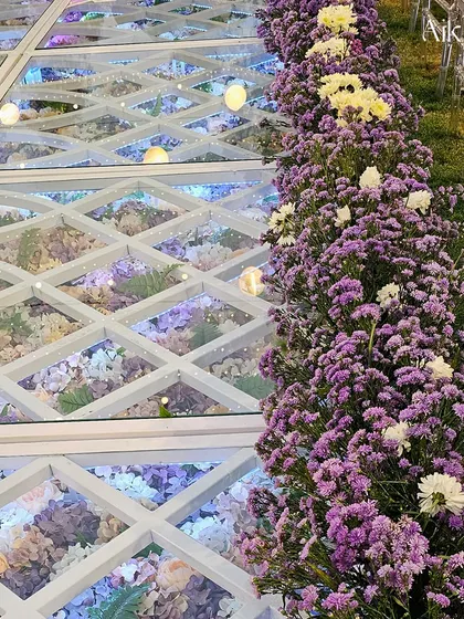 A view of the floral floor from the side, showing how it integrates seamlessly with the surrounding decor and grassy area, bordered by a line of purple flowers.