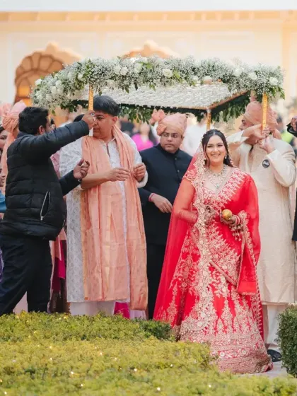 The bride's grand entrance with her family, walking through the palace courtyard. Her happy expression and the beautiful setting make this a perfect documentary moment.