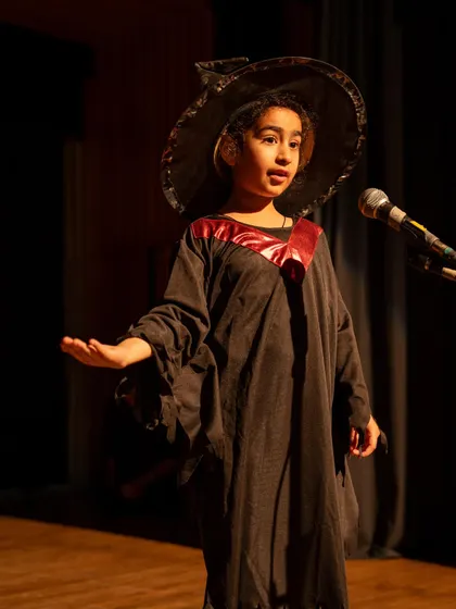 A young witch mid-speech. This shows a strong, confident stance and clear vocal delivery.