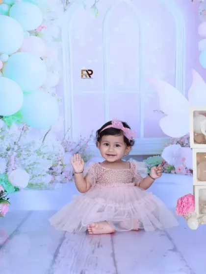 A baby girl in a pink dress sits happily in a fairytale setting, complete with teddy bears, birdcages, and flowers. Her joyful expression is the heart of this magical photo.