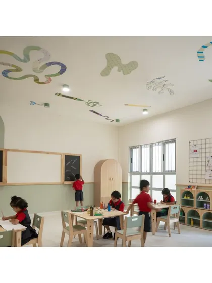 Children engaged in art and writing in a thoughtfully designed classroom. The space features dual whiteboards and blackboards, ample storage in natural wood tones, and playful graphics on the ceiling.
