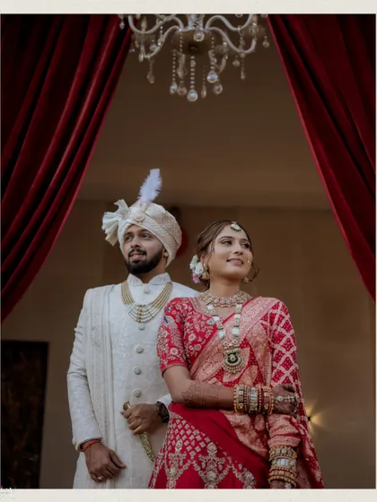 A classic wedding portrait of the couple looking forward, set against dramatic red curtains.
