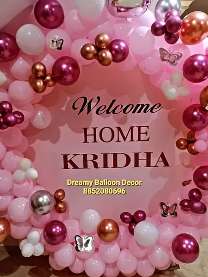 A personalized welcome home ring for a baby girl named Kridha. The pink backdrop is surrounded by a full circle of pink, white, and chrome balloons, with small butterfly details for an extra touch.
