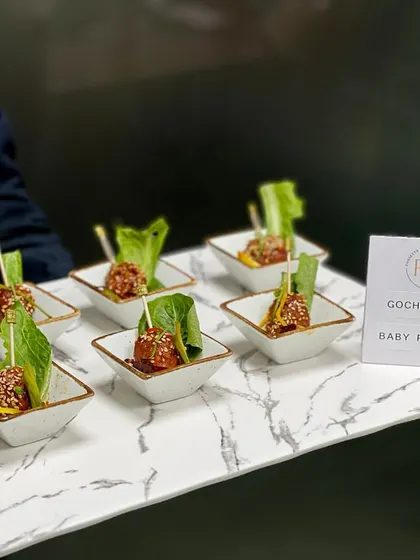 Gochujang Baby Potatoes offer a spicy and savory kick. These Korean-inspired appetizers are skewered for easy handling and served in individual ceramic dishes on a marble-finish tray.