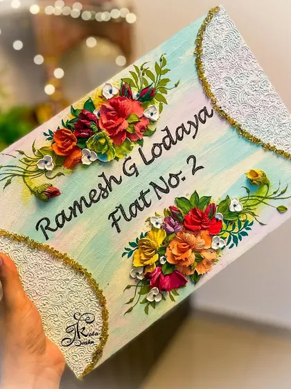 A custom nameplate for "Ramesh G Lodaya," designed with an elegant rectangular shape and curved, textured corners. The multi-colored floral bouquets are arranged to perfectly frame the names.