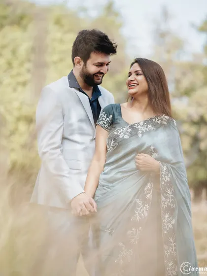 An elegant couple holding hands amidst tall grass. The soft focus on the foreground creates a dreamy effect, drawing the eye to their happy expressions.