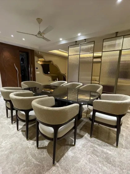 Another angle of the luxurious eight-seater dining set, showing how the curved bouclé chairs complement the strong lines of the black stone table. The fluted glass partition in the background adds texture and divides the space elegantly.