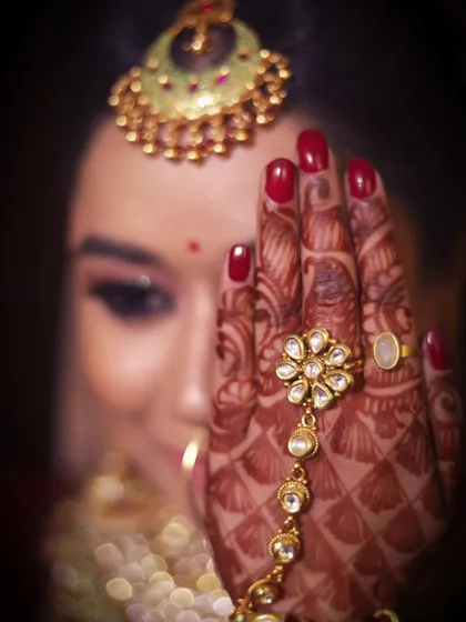 A close-up photo focusing on the bride's hand, showcasing her red nail polish, intricate henna, and beautiful hand jewelry.