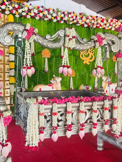 An ornate silver cradle decorated with pink and white flowers, set against a backdrop of banana leaves and traditional motifs. This setup is perfect for a grand naming ceremony.