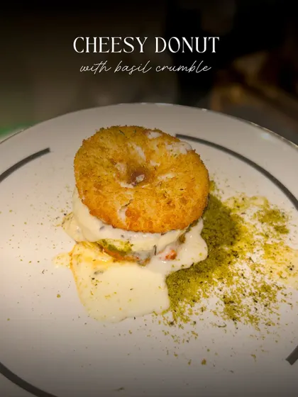 A close-up of my savory Cheesy Donut, filled with molten cheese and topped with a fragrant basil crumble. It's a unique and indulgent appetizer.
