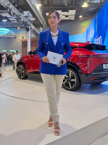 A full-length shot next to the new VinFast VF7. Posing with the product is a key part of being a brand presenter at an auto expo, showcasing the car's design and features.